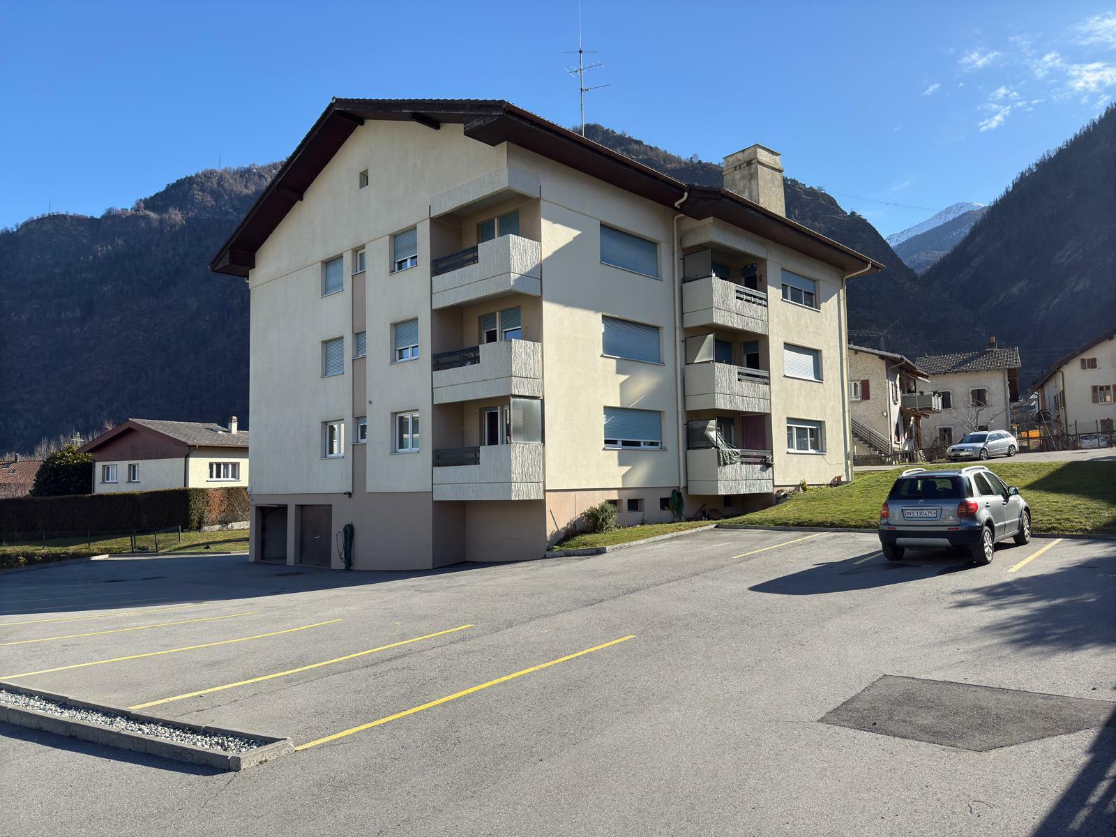 an apartment building with cars in the parking lot and mountains in the background