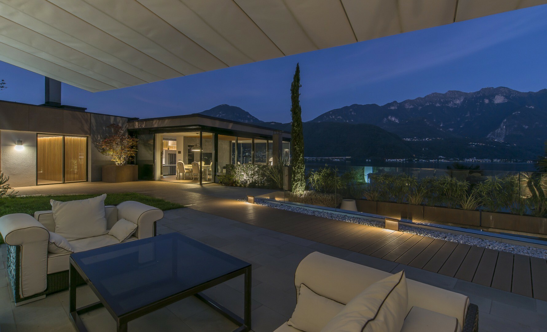 une photo d'une maison moderne avec des meubles d'extérieur sur une grande terrasse surplombant les montagnes la nuit