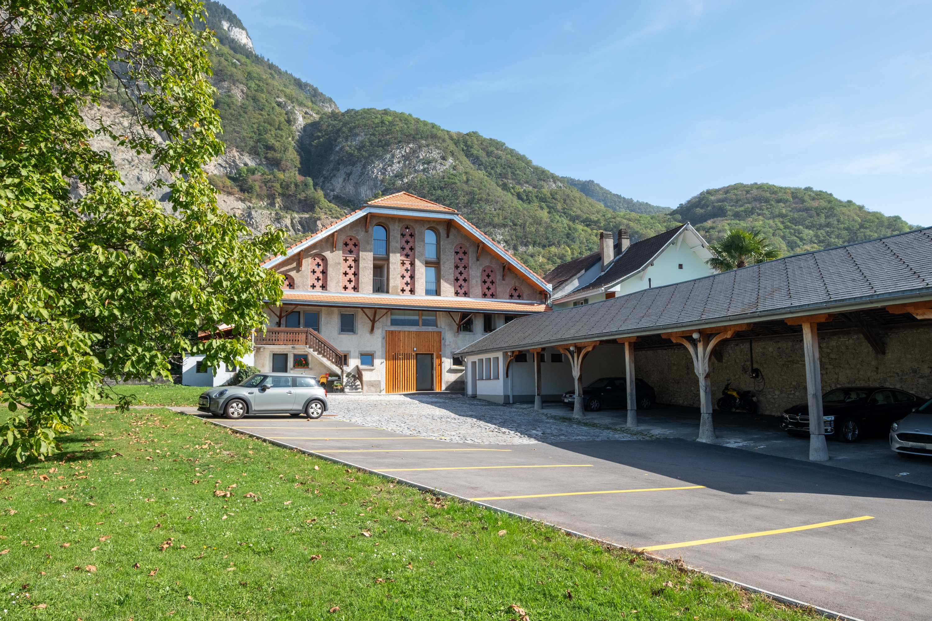 Rénovation d'une ferme du 19e siècle en 15 appartements à Roche : la façade principale et le parking.